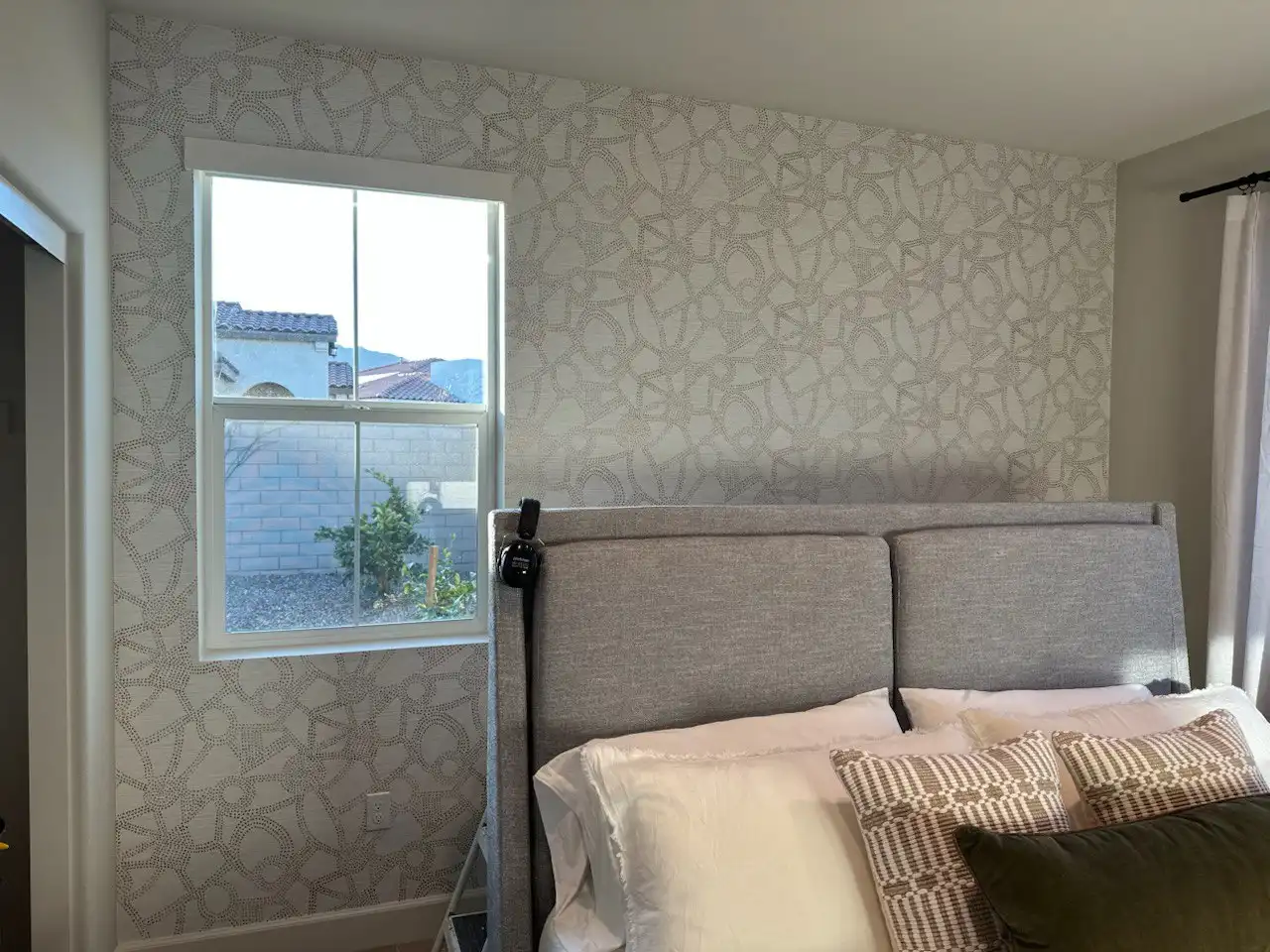 A quiet bedroom with patterned wallpaper behind the bed.