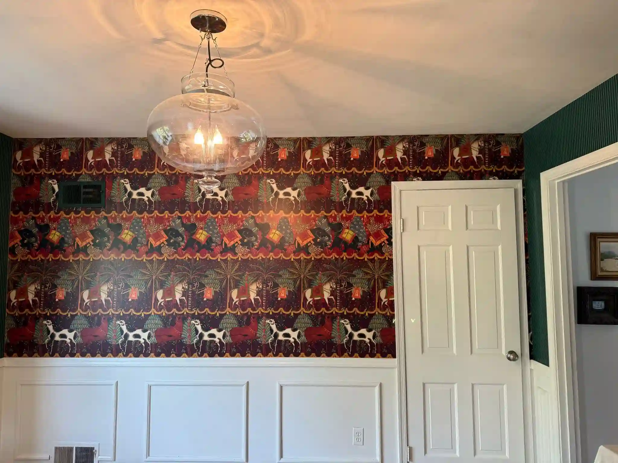 A dining area with a deep red patterned wallpaper above its painted wainscoting.